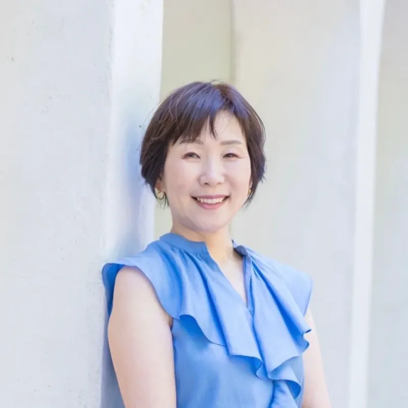 青いフリルトップを着て笑顔でカメラを見つめるショートヘアの女性のポートレート