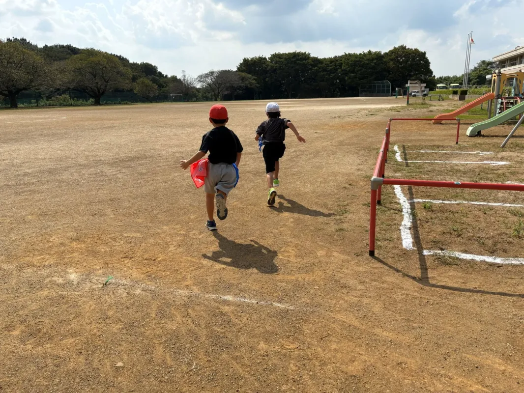 広々とした運動場で、二人の子供が元気いっぱいに走っています