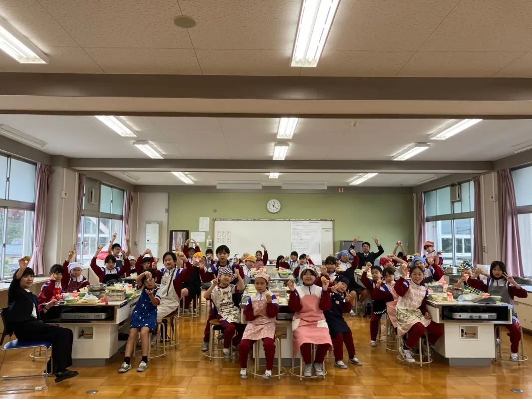 エプロンと三角巾をつけた子どもたちが調理実習室で笑顔でポーズをとっている集合写真