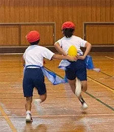 体育館で、体操服と赤白帽を身につけた2人の子供が走っています