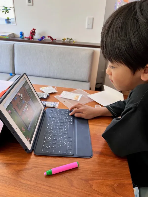 自宅のリビングで、少年がタブレットとキーボードを使ってゲームか学習アプリに集中している様子