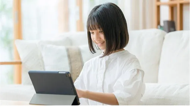 白いシャツを着た笑顔の少女がタブレットを操作している様子