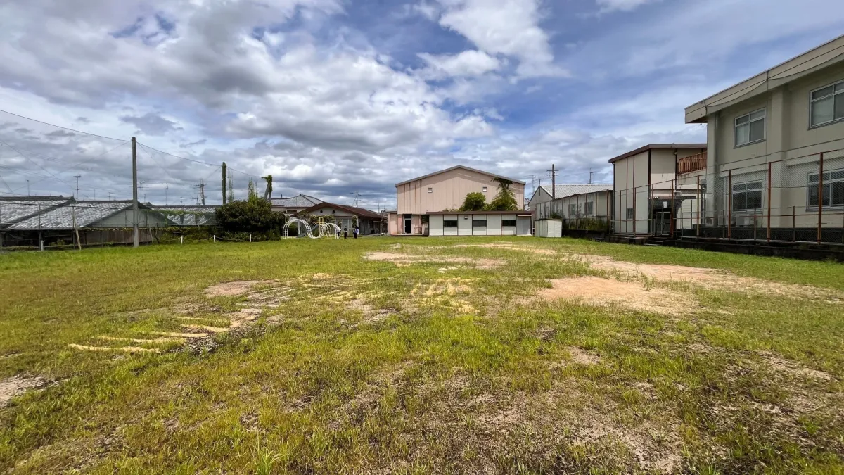 草が生い茂る広々とした野原と、その奥に複数の建物が見える風景