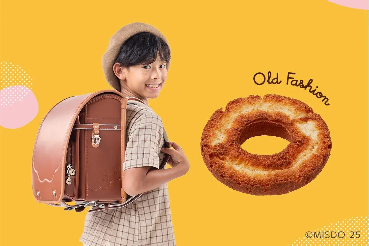 黄色の背景にランドセルを背負いベレー帽をかぶった笑顔の子供と、ミスタードーナツのオールドファッションが並んだ広告画像。