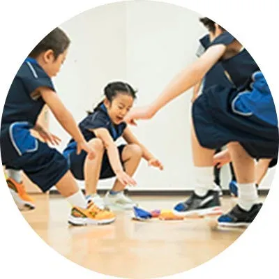 子供たちが室内で何らかの活動に集中している様子。床に置かれたカラフルなものに手を伸ばし、楽しそうにゲームや学習に取り組んでいるように見えます。