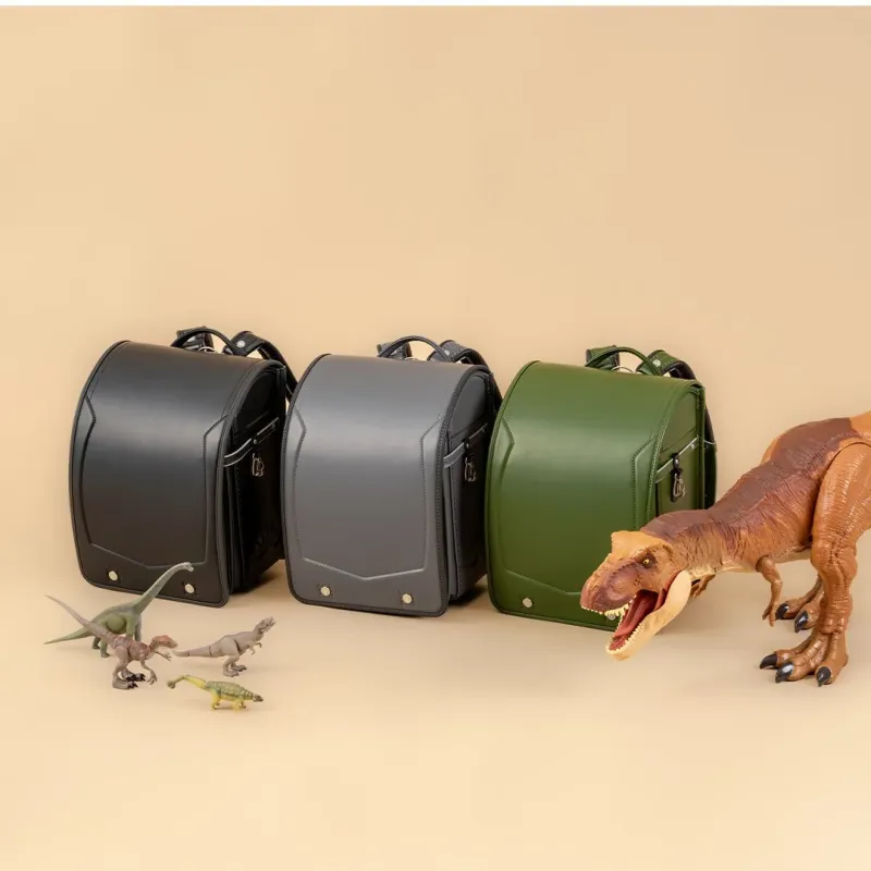 黒、グレー、オリーブグリーンの3色のランドセルが並べられ、その周囲には大小様々な恐竜のおもちゃが配置されています。