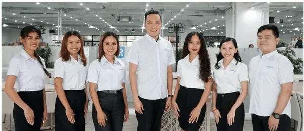 オフィスで働く7人の男女が白いシャツと黒いボトムスを着用し、カメラに向かって笑顔で並んでいる集合写真です。プロフェッショナルな雰囲気が伝わります。