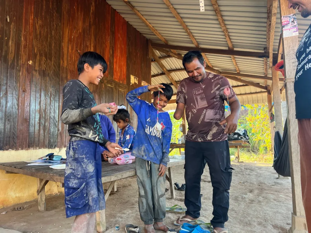 屋外の簡素な建物の下で、子供たちが笑顔で大人たちと交流している様子