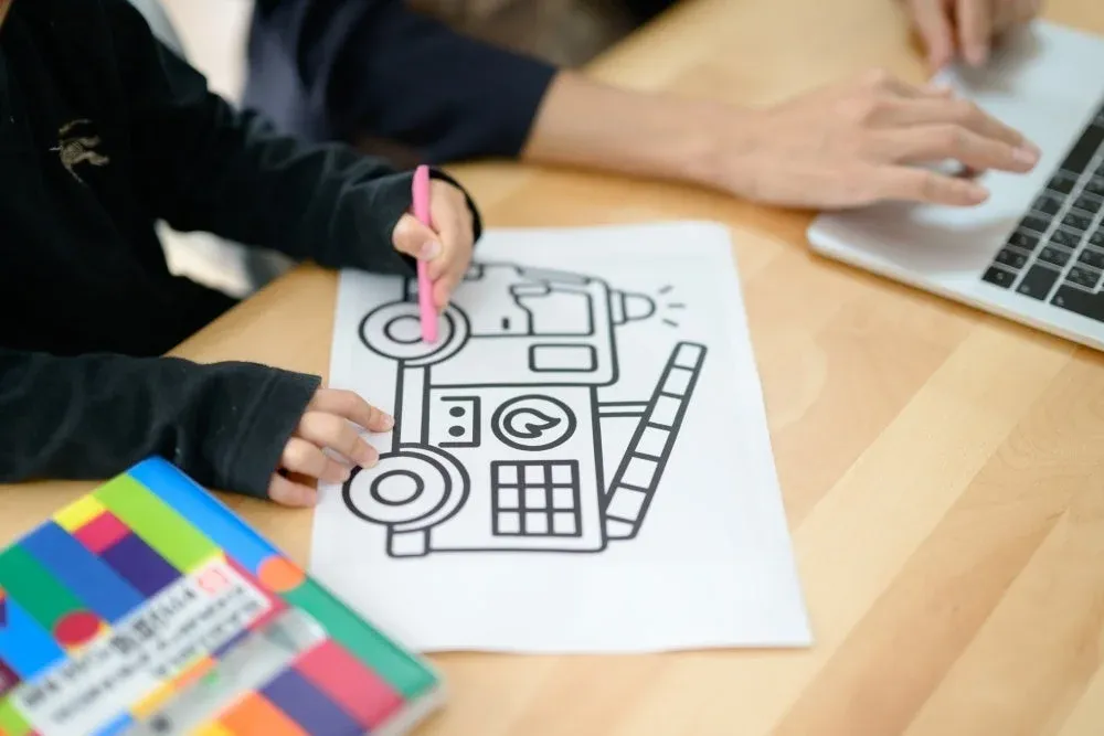 木製デスクで塗り絵をする子供とノートパソコンを操作する大人