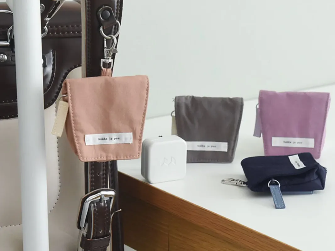 複数のカラフルなミニポーチやキーホルダーが写っています。一部はバッグに付けられ、一部は白い棚の上に置かれており、それぞれに「kukka ja pau」というロゴが入っています。