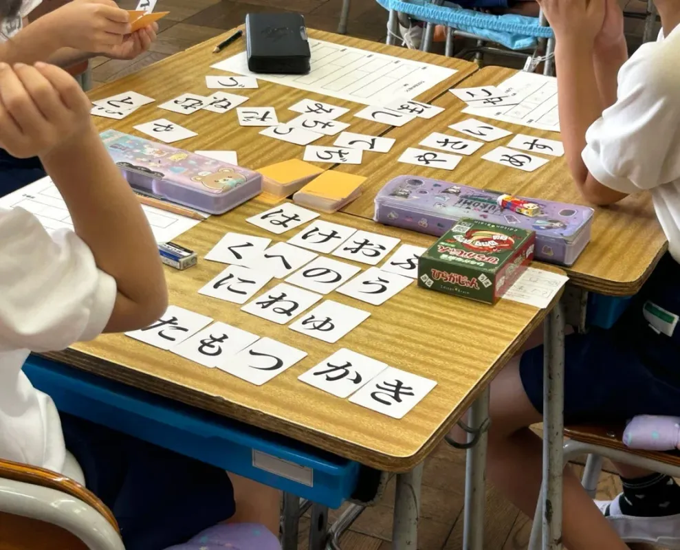 木製の机を囲んで座る子どもたちが、ひらがなのカードを使って学習している様子