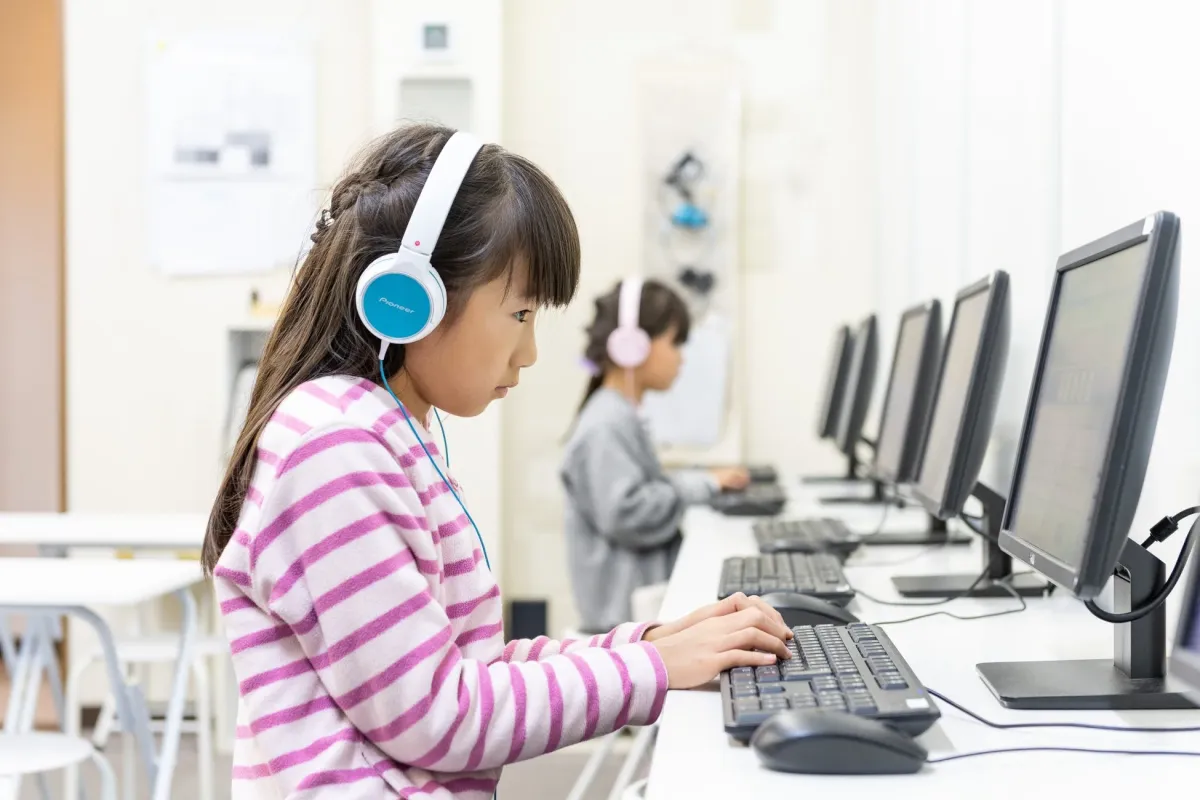 ヘッドホンをつけた女の子たちがパソコン学習に取り組む様子