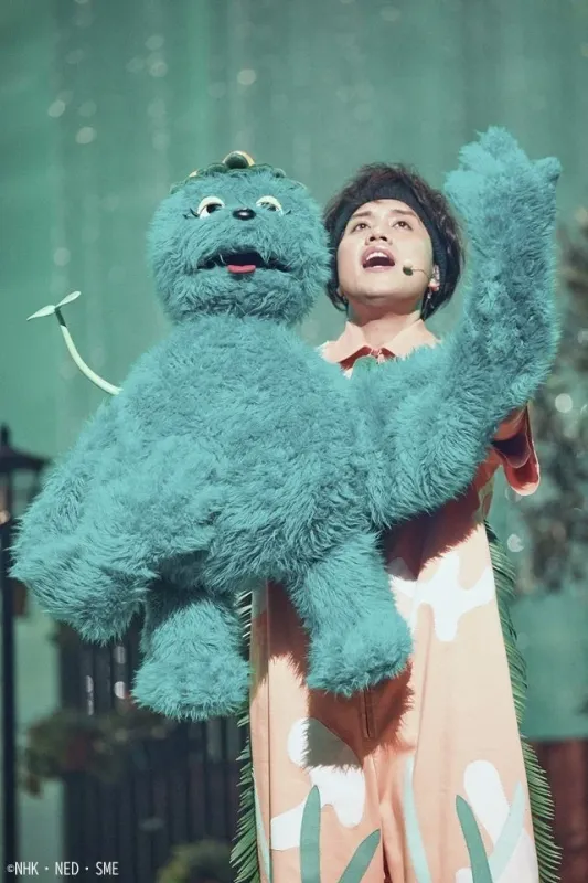 青い毛むくじゃらの大きなキャラクターと、マイクを付けた人物がパフォーマンスをしている様子