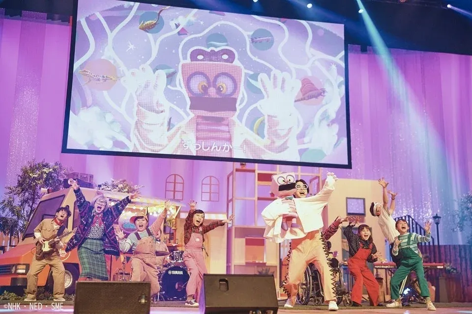 ステージ上で複数の出演者が楽器を演奏し、歌い踊るライブパフォーマンスの様子