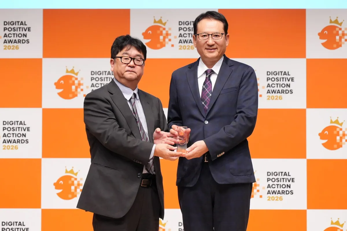 DIGITAL POSITIVE ACTION AWARDS 2026の授賞式で、スーツ姿の二人の男性がトロフィーを授受している様子です。