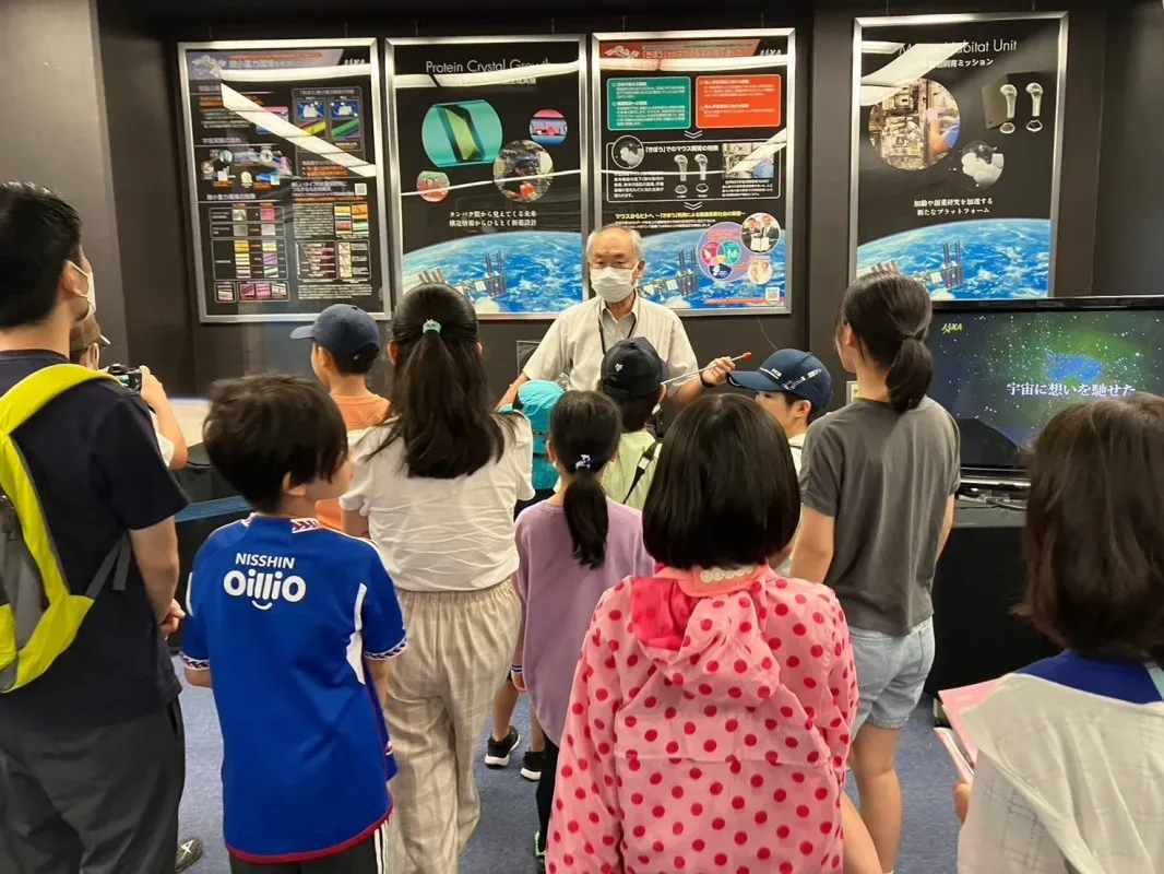JAXA展示会で説明を聞く子どもたち