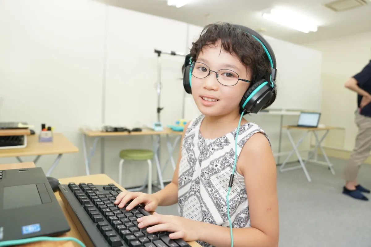 眼鏡とヘッドホンを着用した若い女の子がパソコンのキーボードを操作している