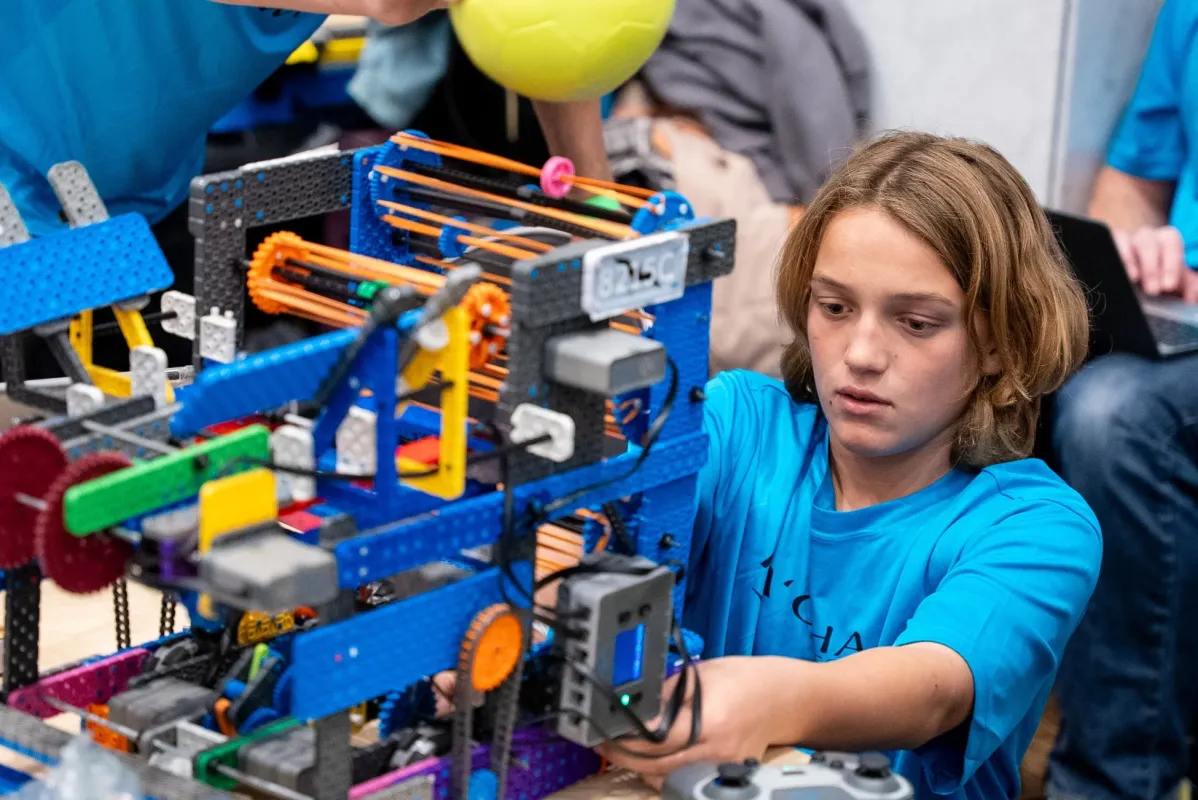 青いTシャツを着た少年が、カラフルで複雑なロボットを真剣な表情で操作または調整しています。