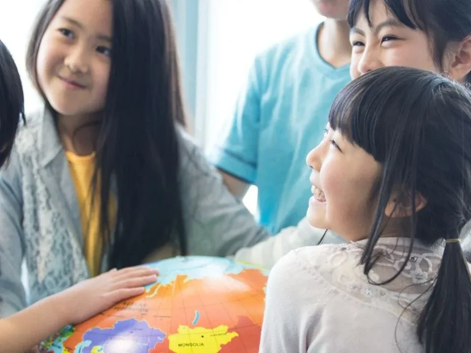 地球儀を囲んで集まるアジア系の子供たちが笑顔で学習している様子。