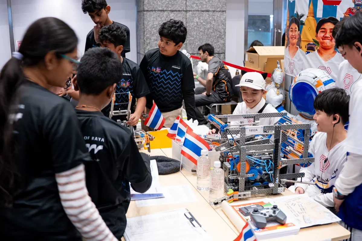 タイの学生たちがロボット競技会に参加している様子。複数のチームがそれぞれのロボットを囲み、真剣な表情で作業や議論を行っている。