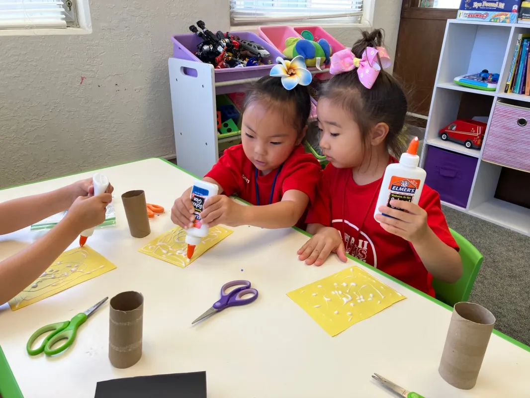 二人の幼い女の子がテーブルで工作活動に集中しています。