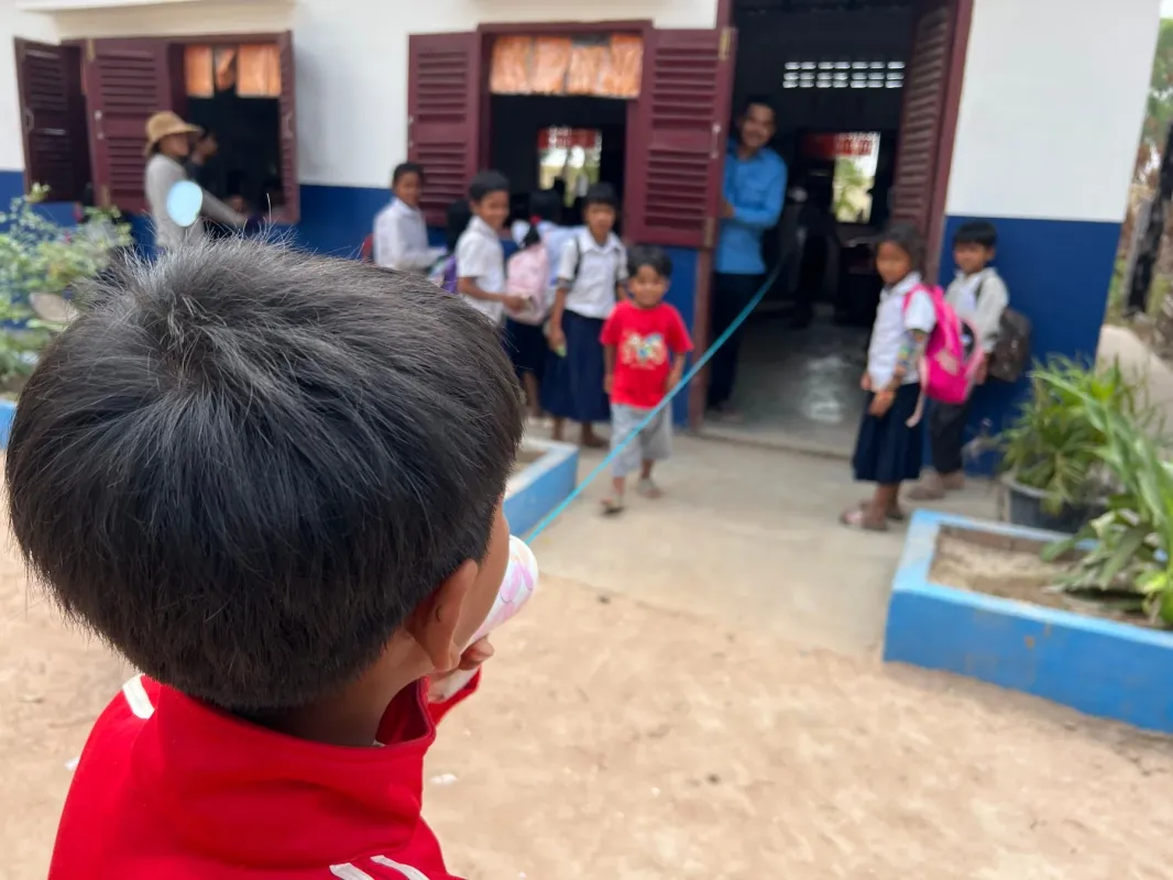 学校のような建物の前で、制服姿の子供たちが集まっています。