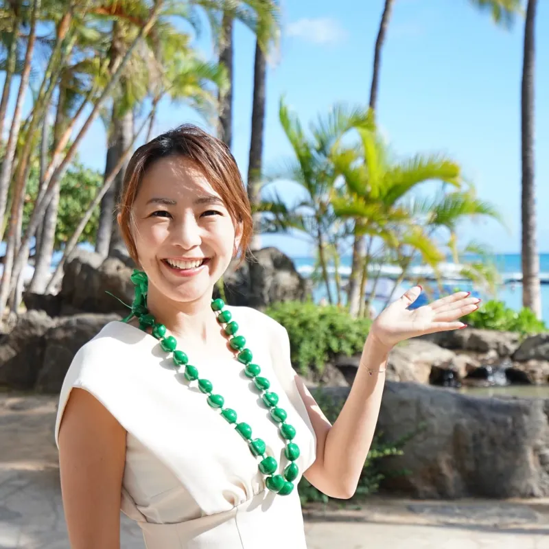 笑顔の女性が緑のレイを身につけ、手のひらを広げています。